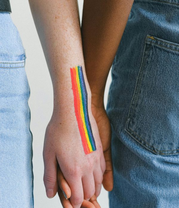 A close-up of an interracial couple holding hands with a rainbow drawn on the wrist, symbolizing LGBTQ pride.